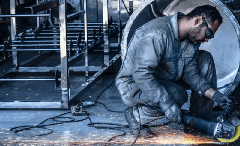 Crisi metalmeccanica: un lavoratore taglia un pezzo di metallo in una luce grigia