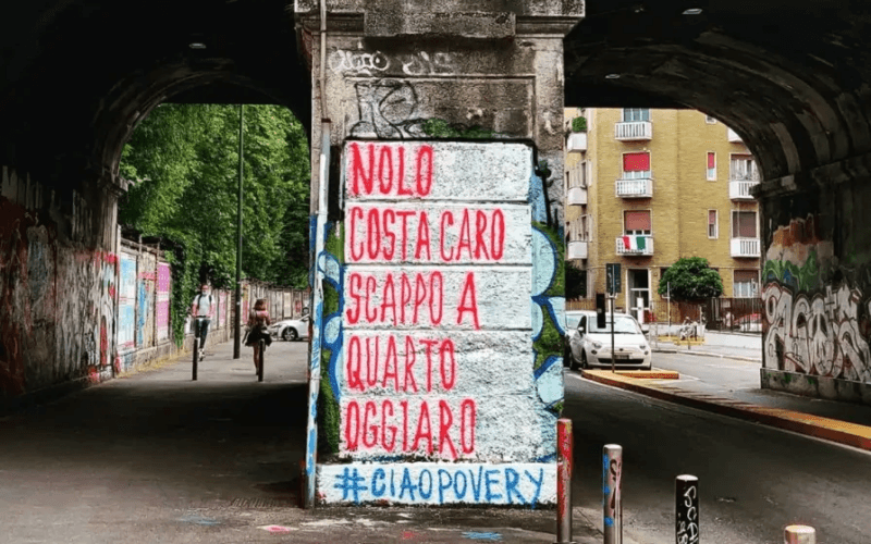 Milano e lavoro, un cartello sulla povertà vicino a un cavalcavia