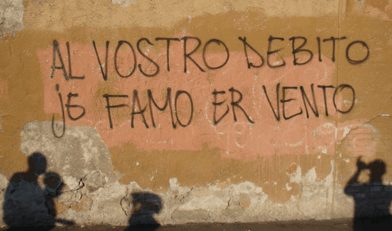 Una scritta sul debito su un murale in Grecia: "Al vostro debito je famo er vento"